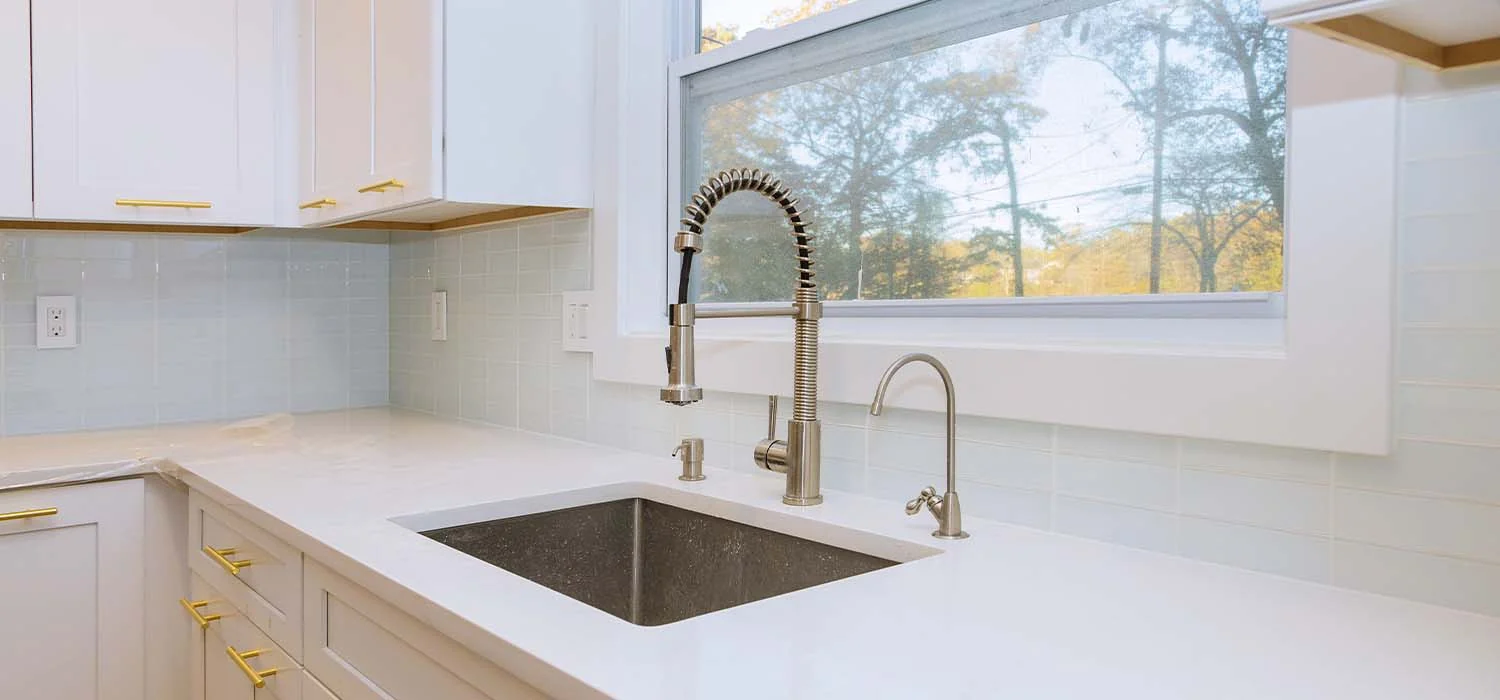 Modern white kitchen sink area with a stainless steel pull-down faucet and light blue tiled backsplash.